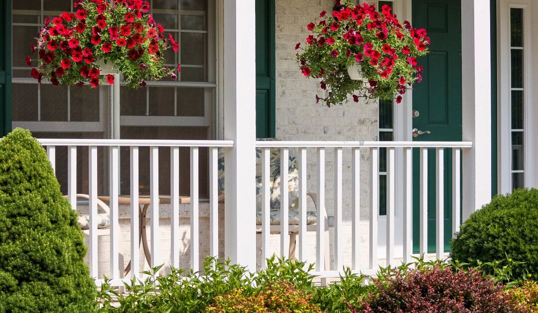 A front porch with a white hand railing. There are multiple plants in front of and hanging above the porch.