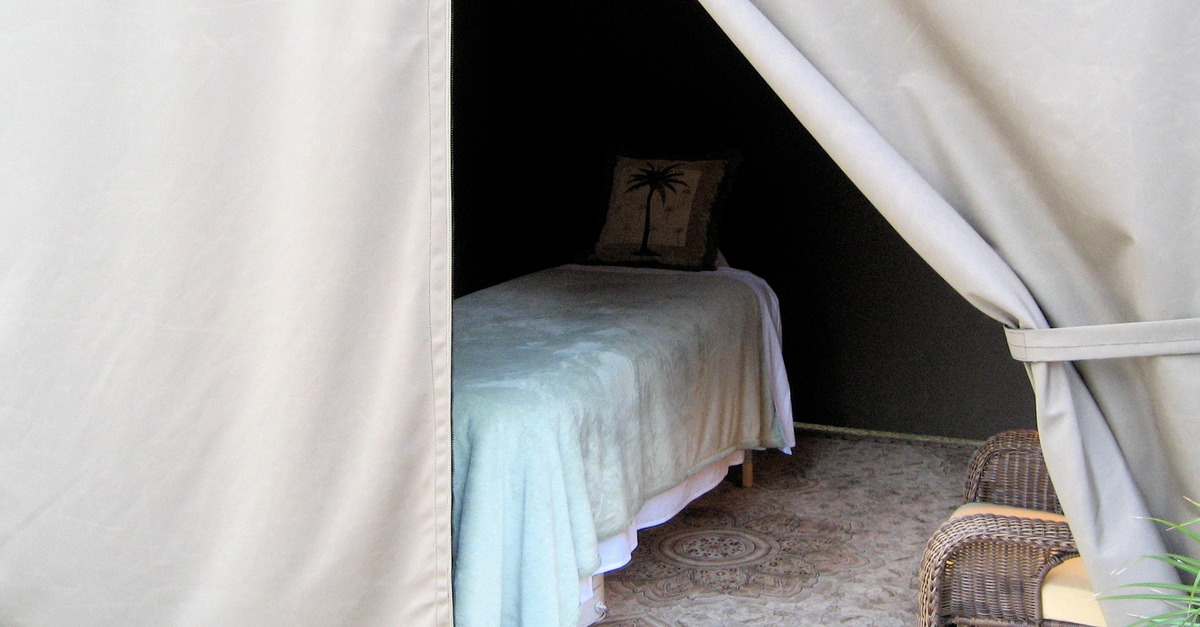 A cabana with tan-colored drapes. The front drape is partially open, revealing a massage table and two wicker chairs.